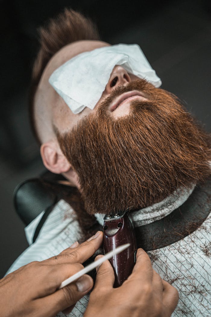 Close-up of a man's beard being trimmed by a barber in a barbershop setting.